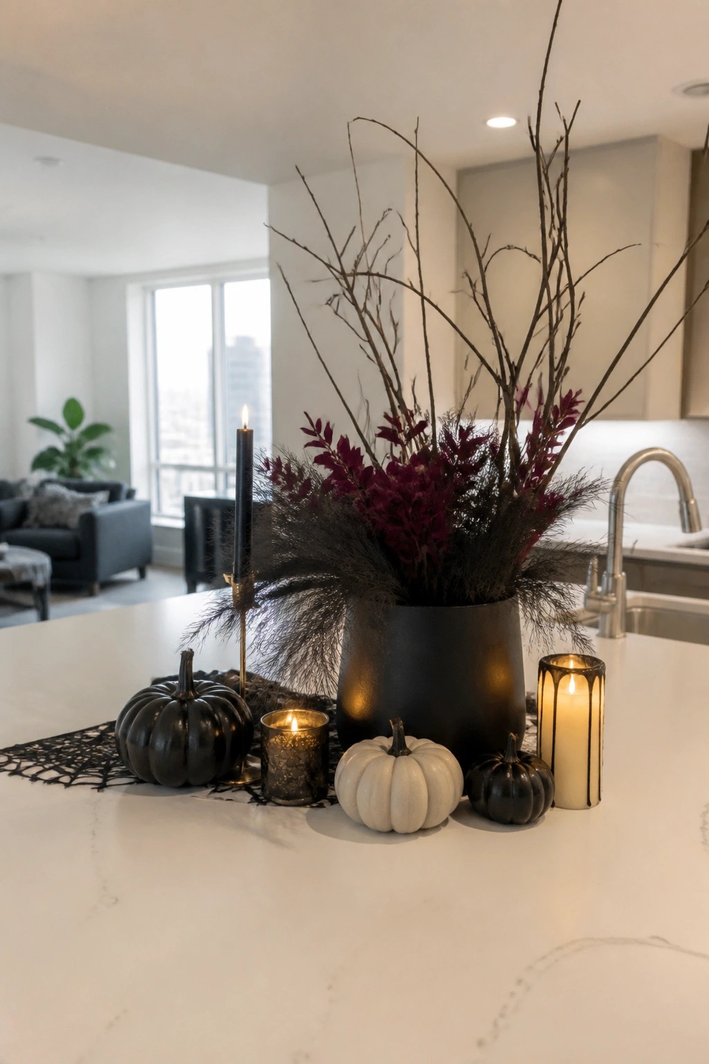 Kitchen island decorated with a black vase of tall bare branches and dark foliage, surrounded by black and white pumpkins and lit candles.