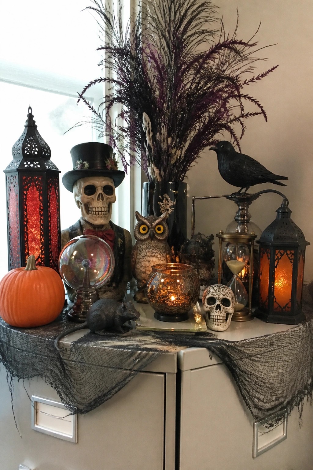 Office cabinet decorated with a skeleton wearing a top hat, a black crow figurine, skulls, glowing lanterns, and dark branches.
