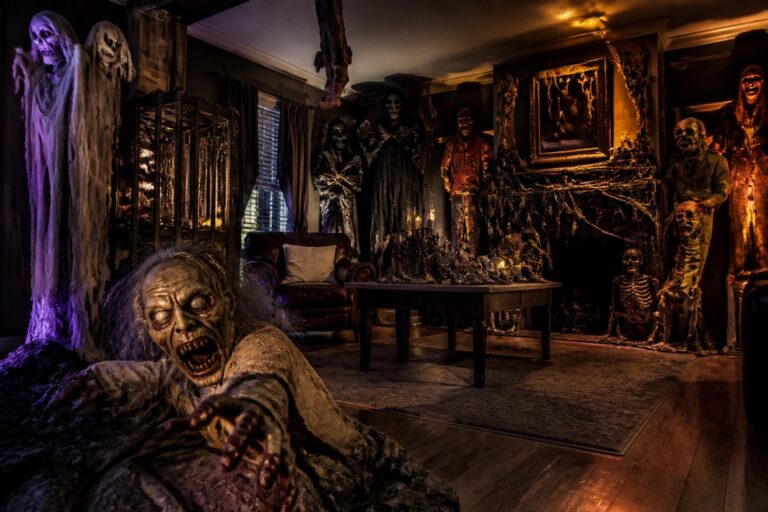 Living room decorated for Halloween with a large horned skeleton figure holding a staff, smaller skeletons seated and hanging, spiderwebs, and lanterns around the space.