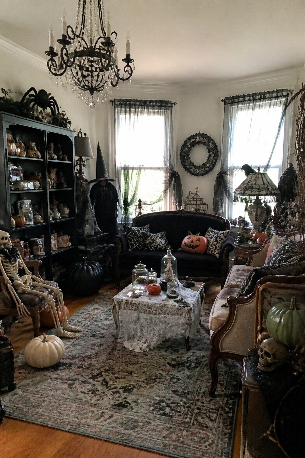 Living room with multiple decorative skeletons posed in chairs and on the floor, along with jack-o'-lanterns, a witch figure, and spiders on furniture.