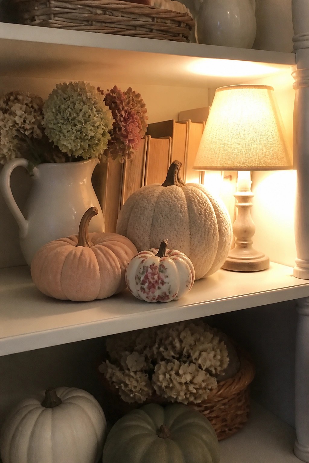 Built-in shelves decorated with assorted neutral pumpkins, a white pitcher of dried flowers, books, and a small lamp.