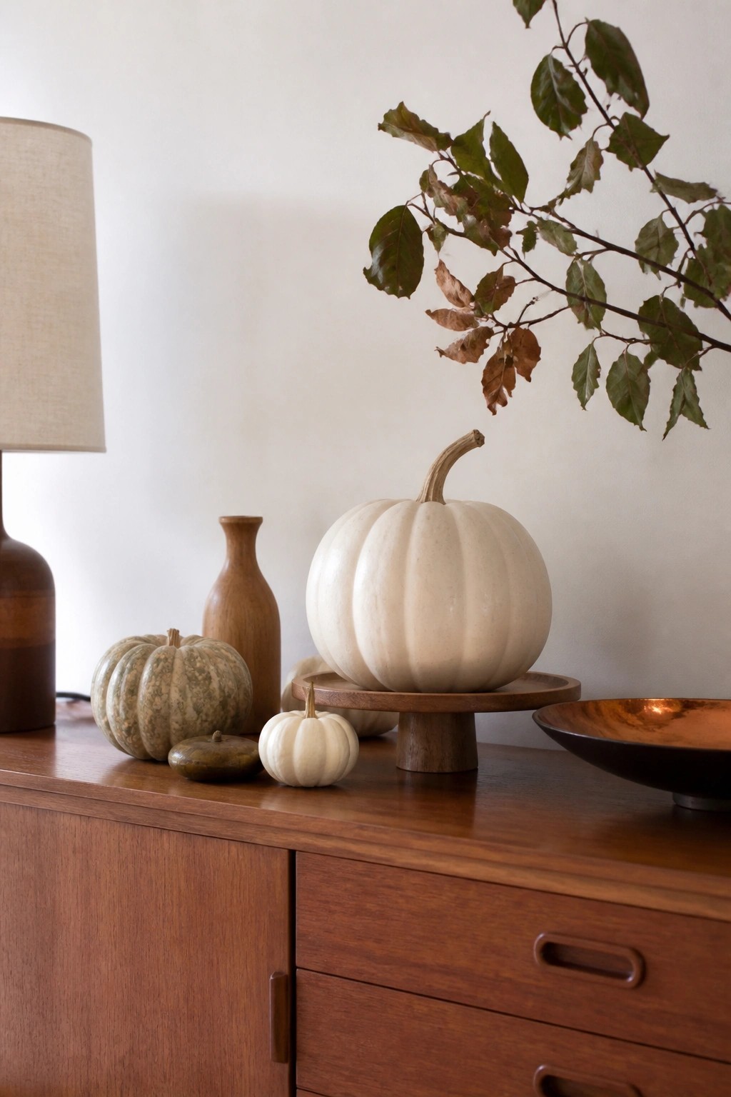 Wooden console table styled with assorted white and green pumpkins, including one large white pumpkin on a wooden stand.