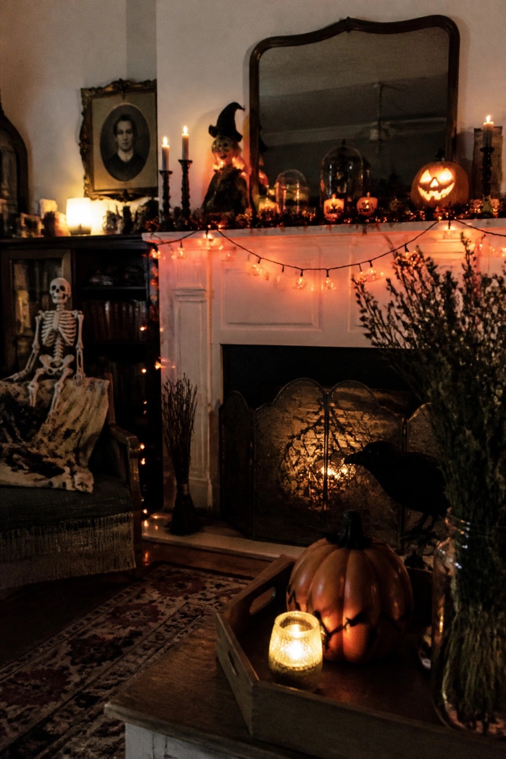 A white fireplace mantel decorated with glowing jack-o'-lanterns, string lights, candles, and a small witch figure for Halloween.