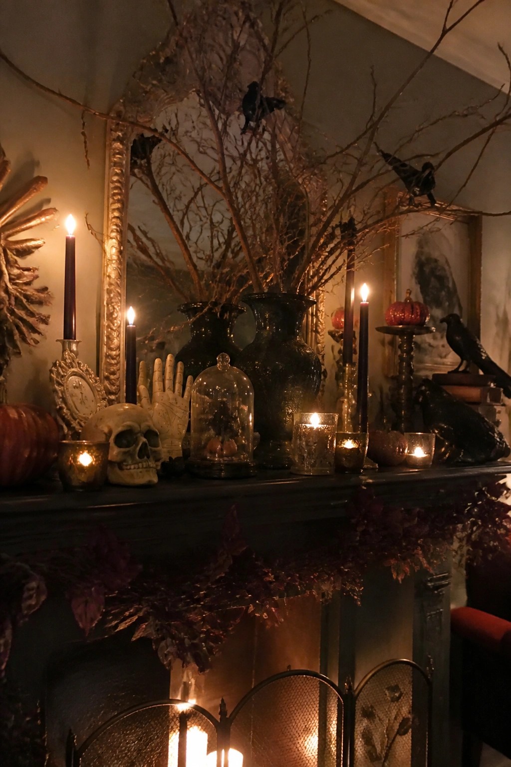 A dark fireplace mantel arranged for Halloween with black branches in vases, a skull, black crows, candles, and small pumpkins.