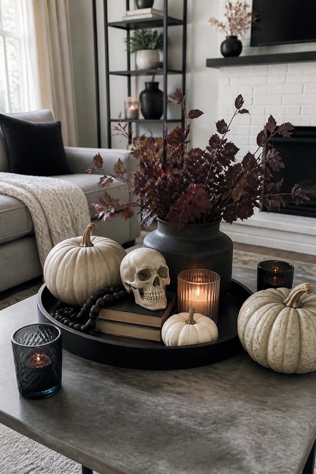 Coffee table tray holding a decorative skull, white pumpkins, stacked books, a lit candle, and dark foliage in a black vase.