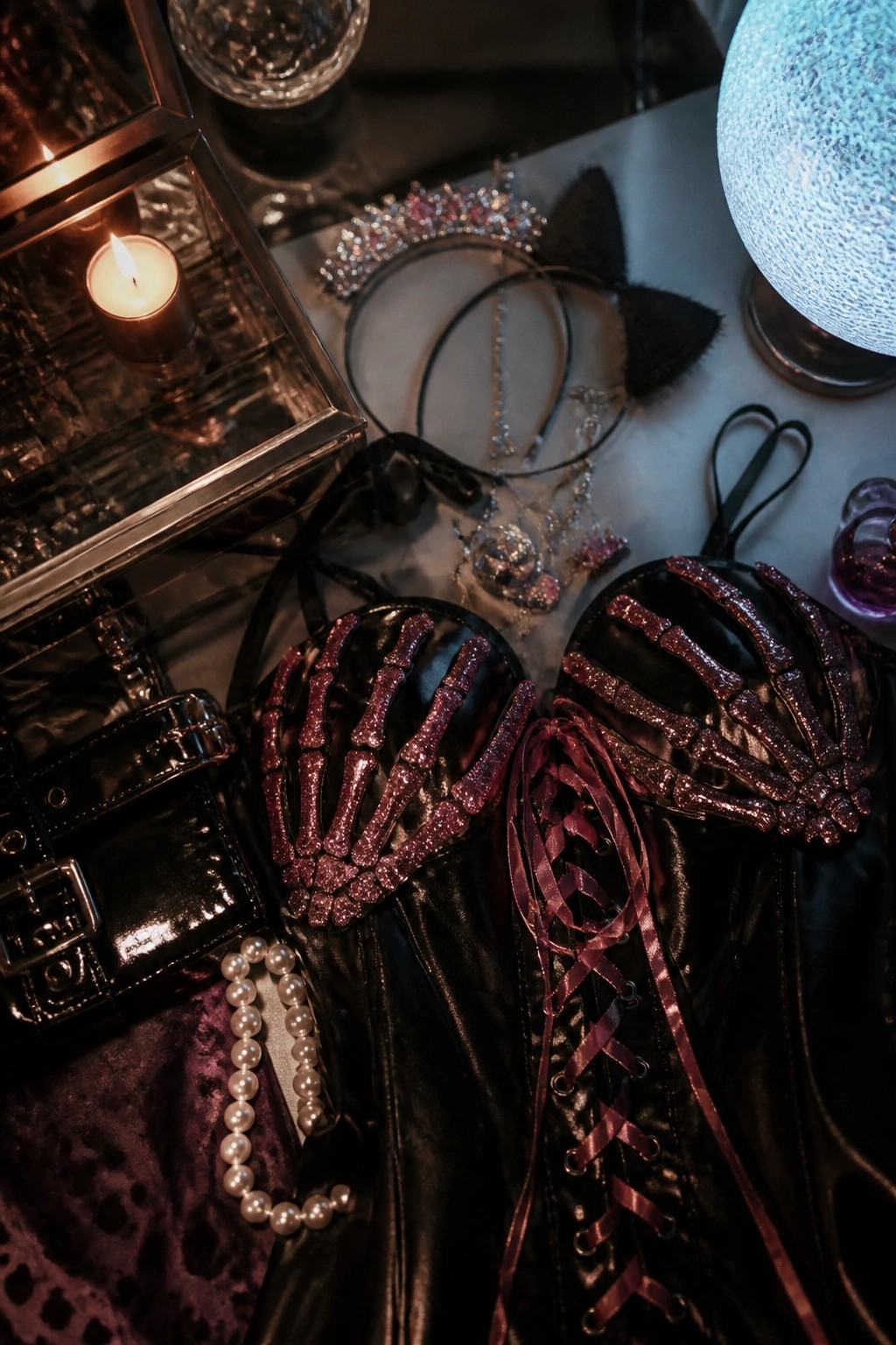 Black corset top with glittery skeleton hand details arranged with a tiara, cat ears, pearl necklace, and lit candle on a tabletop.