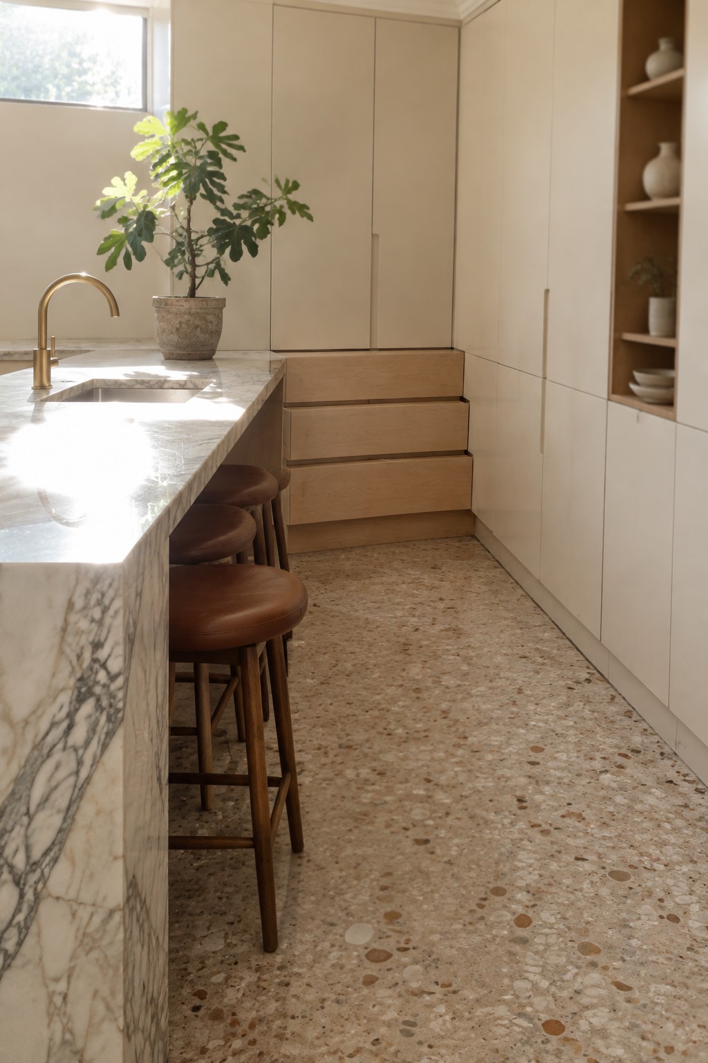 A narrow kitchen with flush beige cabinets, a marble island, and a built-in corner cabinet section.