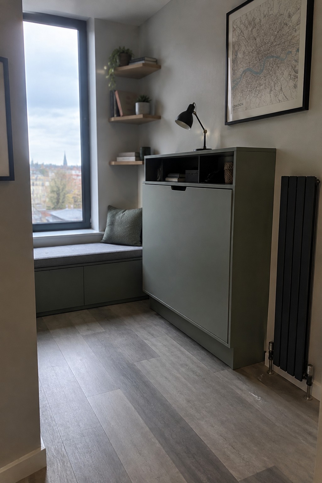 A tall gray-green cabinet with open upper cubbies and a closed lower door stands beside a window seat in a narrow room.