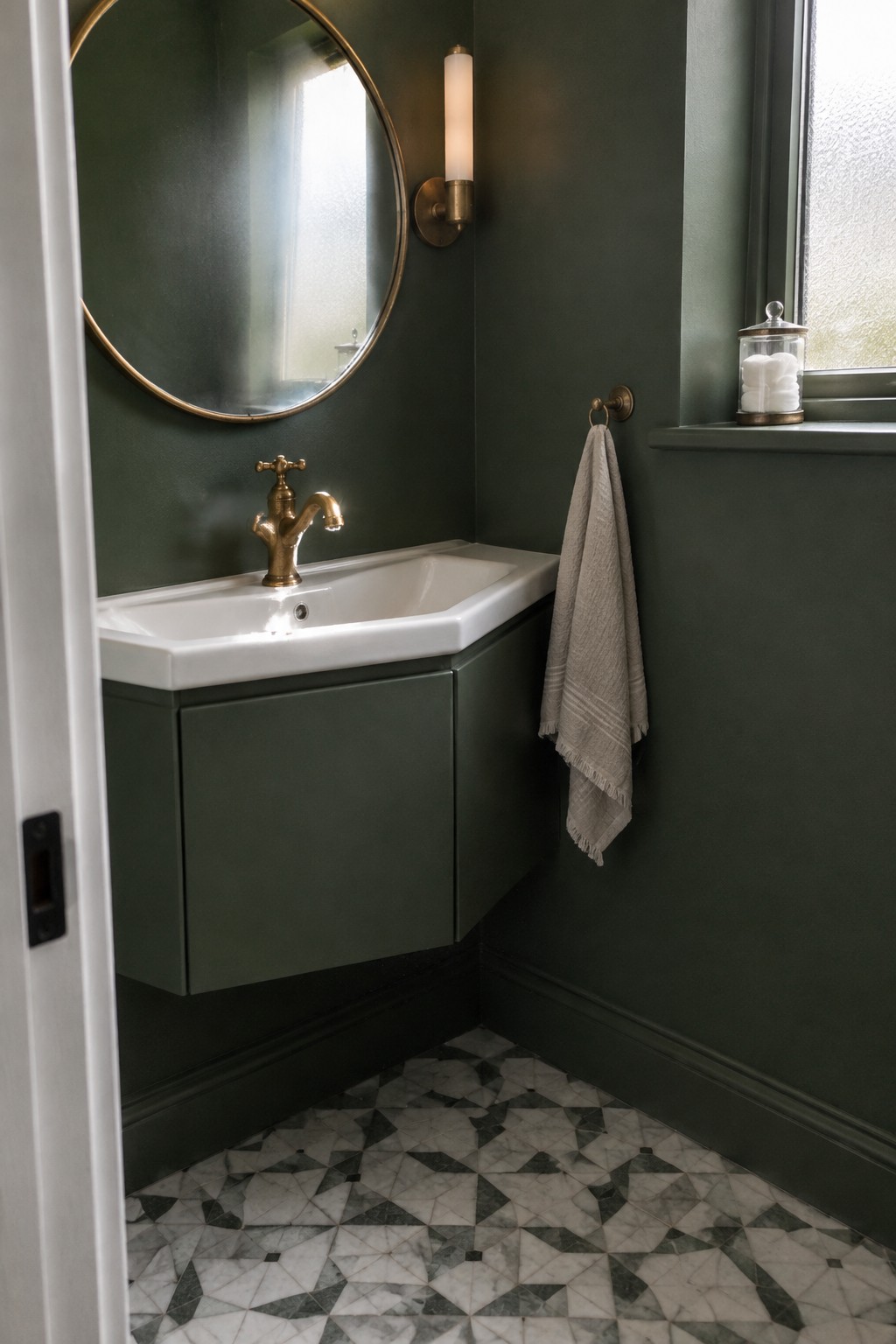 A dark green corner vanity cabinet with a white sink sits beneath an oval mirror in a small bathroom.